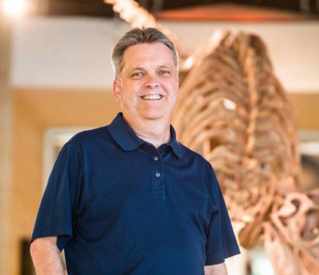 Dr.-Donham protrait in front of a dinosaur structure.